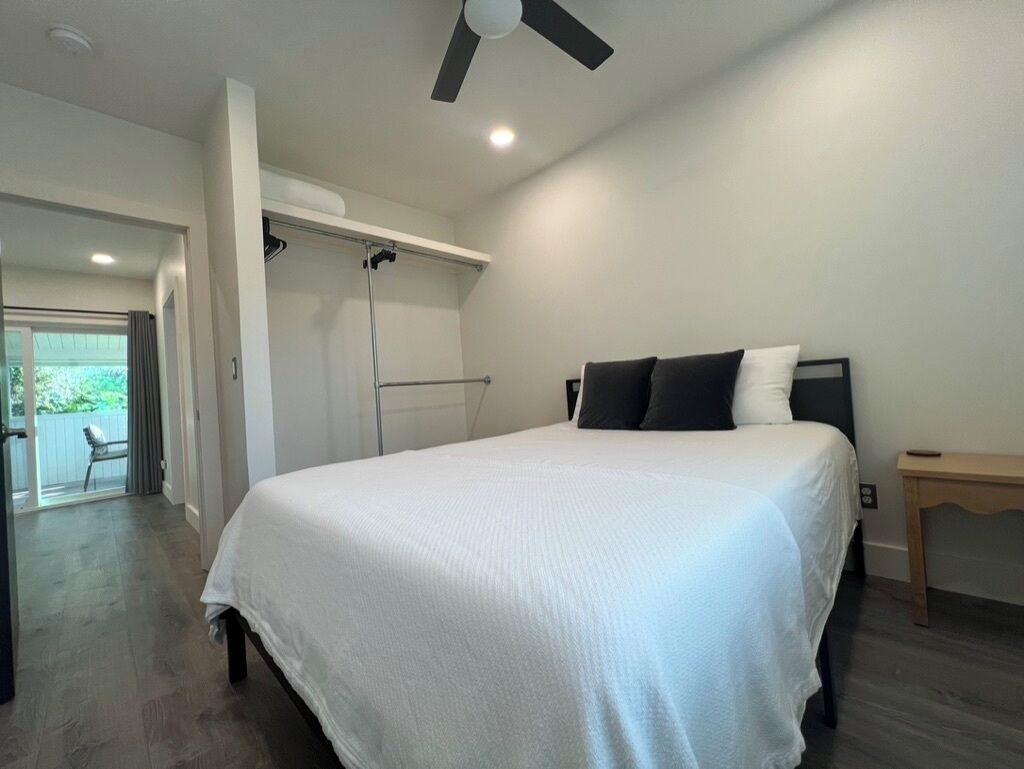 A bedroom with a bed, a ceiling fan, a window, and a door leading to a balcony.
