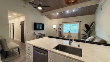 A modern kitchen with a marble countertop, built-in dishwasher, and a ceiling fan.