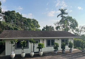 A single-story building with a dark roof and white walls, surrounded by potted plants and trees. - Spacious 3-bedroom house with AC in charming Kailua-Kona (Kailua-Kona)