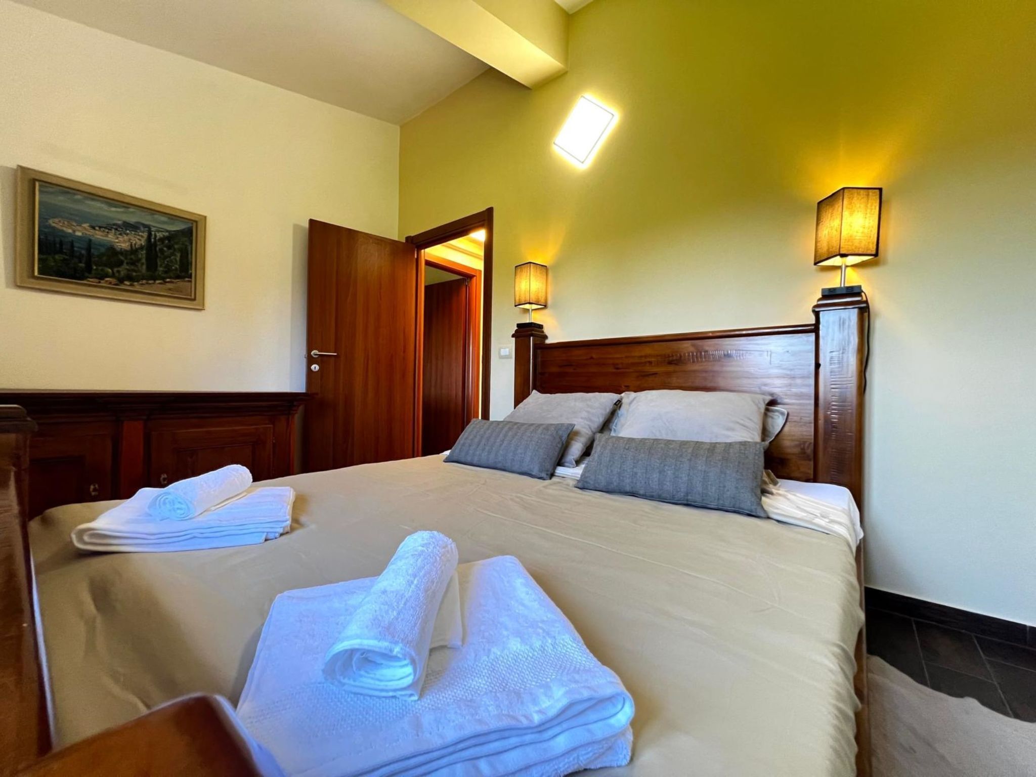 Une chambre d’hôtel avec un lit, deux lampes de chevet, une porte, un tableau au mur et une serviette pliée sur le lit.