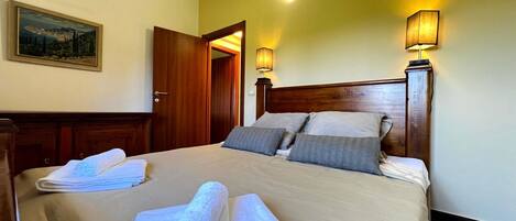 Une chambre d’hôtel avec un lit, deux lampes de chevet, une porte, un tableau au mur et une serviette pliée sur le lit.