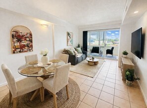 Ein modernes Wohnzimmer mit einem Glastisch, einer Couch und einem an der Wand befestigten Fernseher.