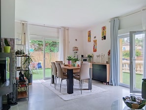 A modern dining area with a glass door leading to a garden, a dining table with chairs, and a kitchen area with a counter and cabinets. - Villa Le Cercle by Interhome (Saint Paul de Vence)