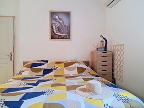 A bed with a geometric patterned bedspread, a wall-mounted clock, a framed artwork, and a tall, narrow cabinet with drawers. - Villa Le Cercle by Interhome (Saint Paul de Vence)