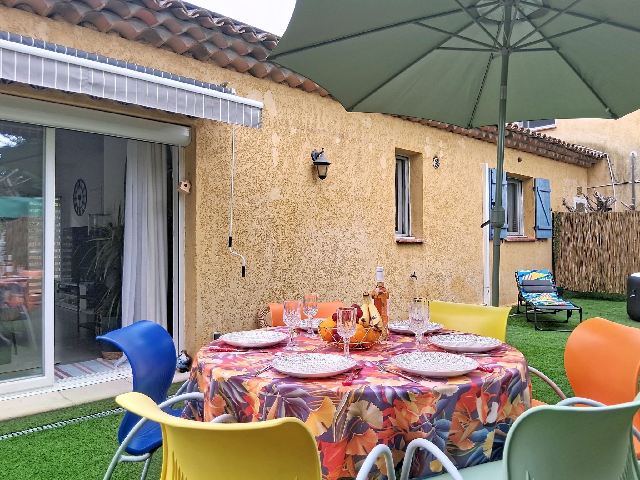 A patio with a table set for dining, outdoor chairs, a large umbrella, and a view of a building with a tiled roof.