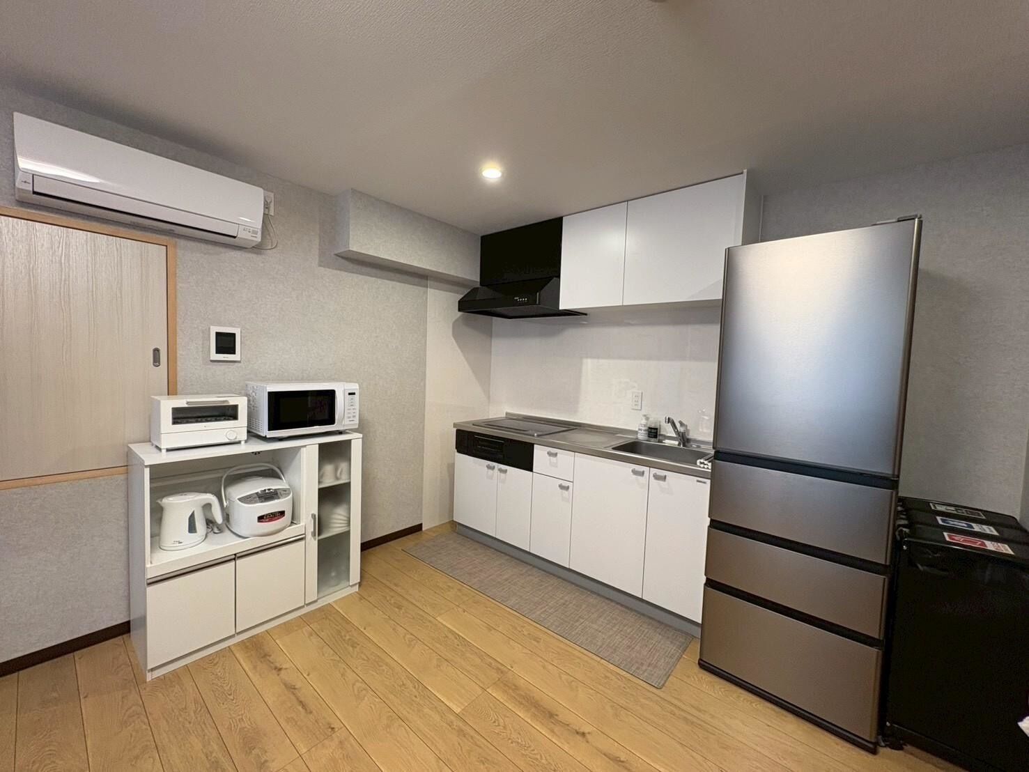 A compact kitchen with a microwave, toaster, and refrigerator, wooden flooring, and a small window.