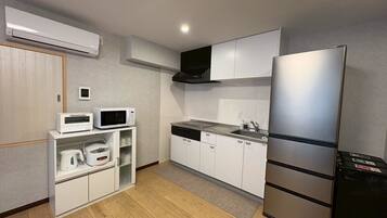 A compact kitchen with a microwave, toaster, and refrigerator, wooden flooring, and a small window.