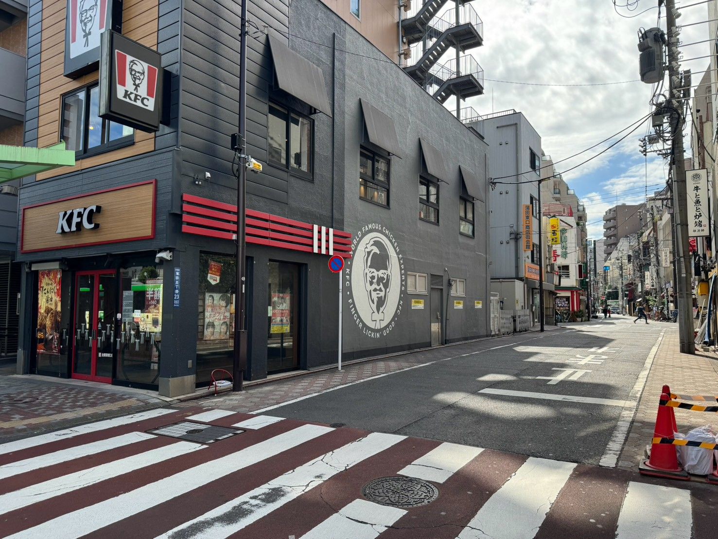 Een KFC restaurant op een kruising in de stad, met een voetgangersoversteekplaats en verkeerslichten.