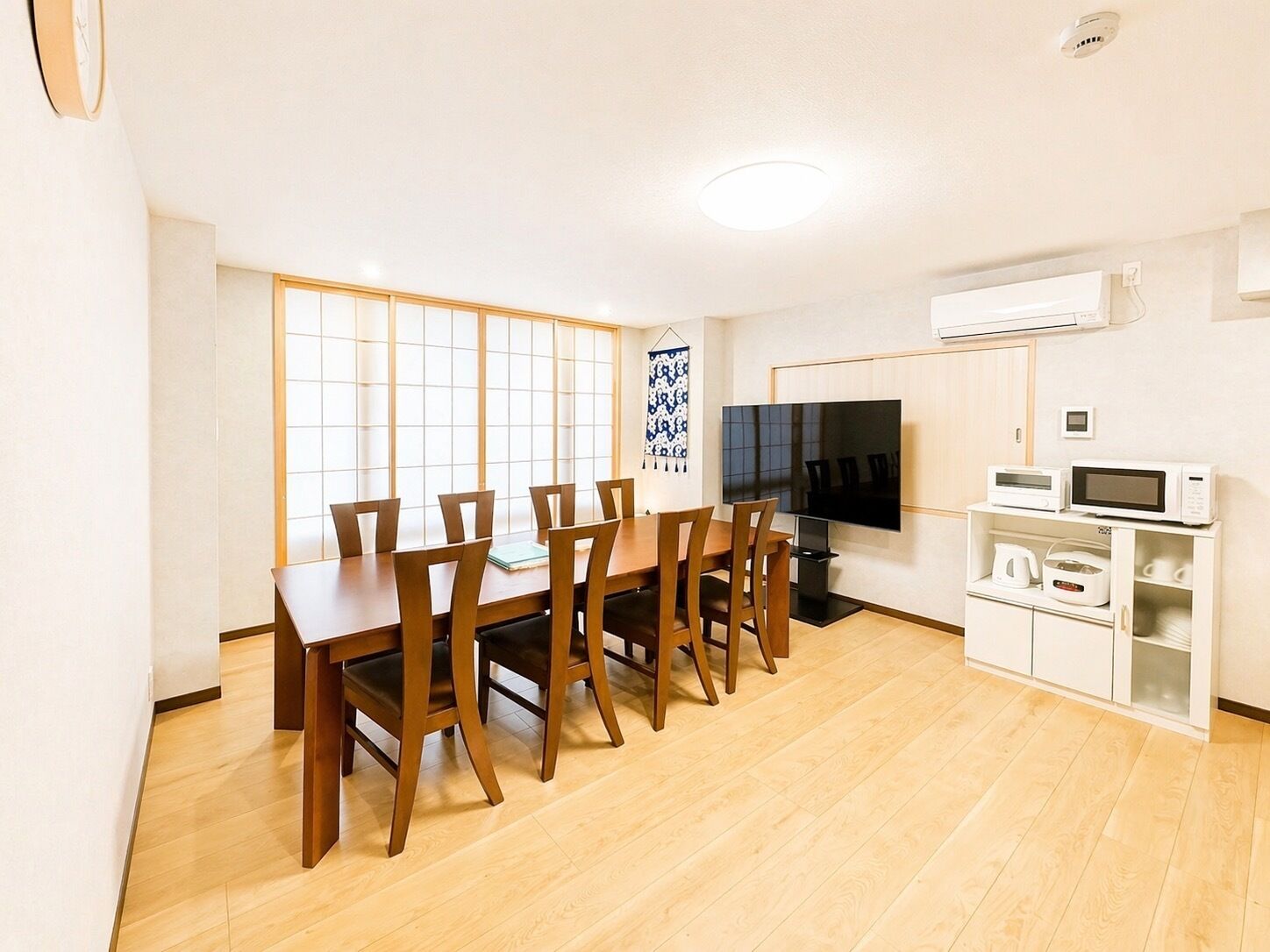 A dining area with a wooden table and chairs, a flat-screen TV, and a microwave on a cabinet.
