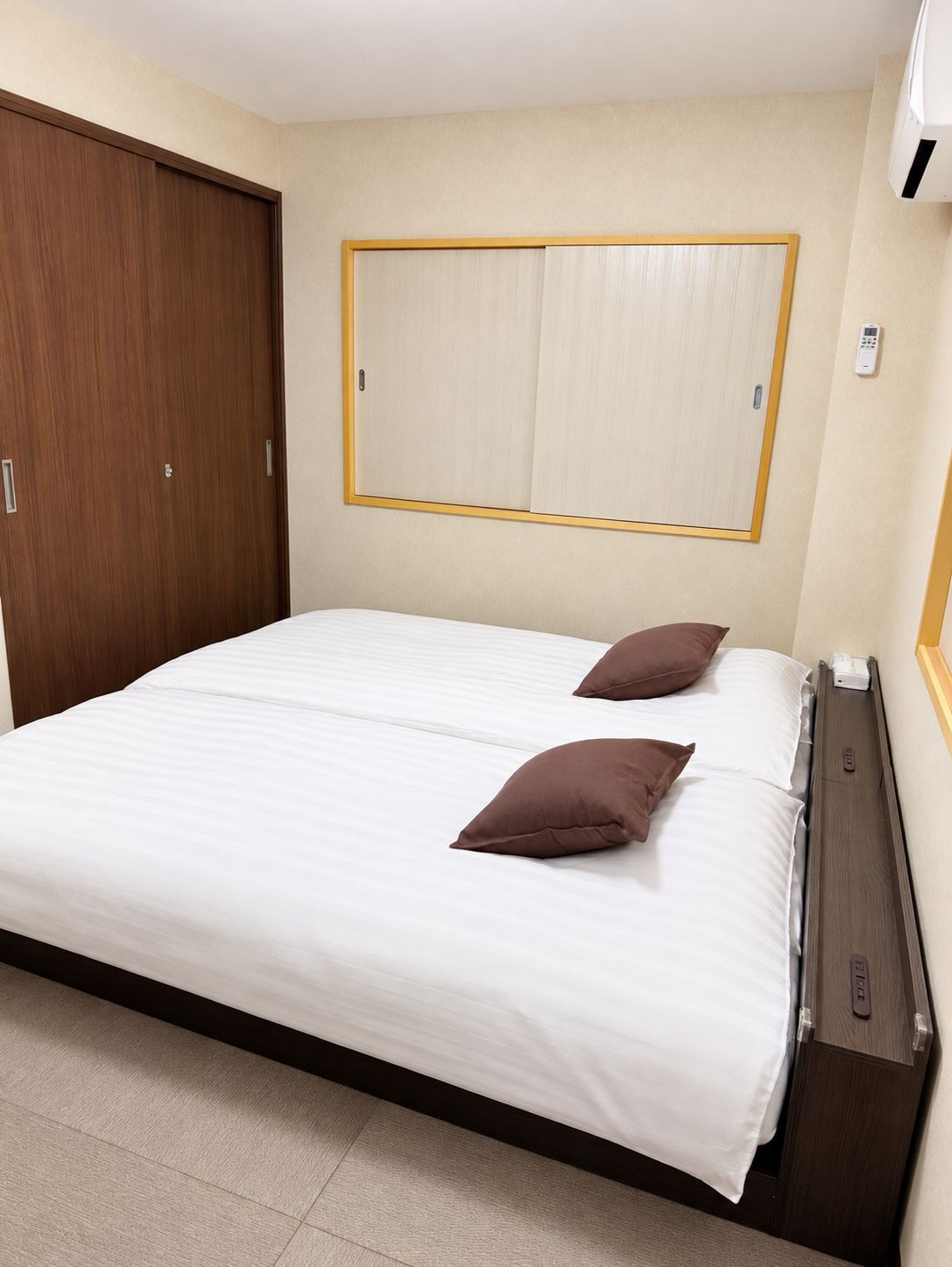 A hotel room with a bed, two pillows, a wardrobe, and a wall-mounted heater.