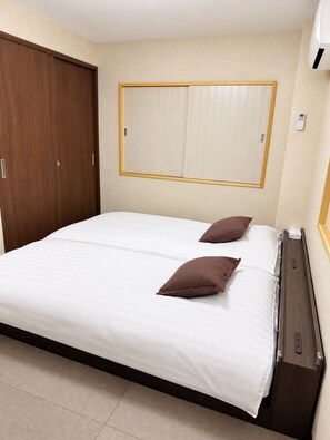 A hotel room with a bed, two pillows, a wardrobe, and a wall-mounted heater. - Right next to the JR Kamata East Exit; right in front of the Kamata East Exit terminal bus stop from Haneda Airport—YU'SHOUSE 3, newly renovated and open! (大田区)