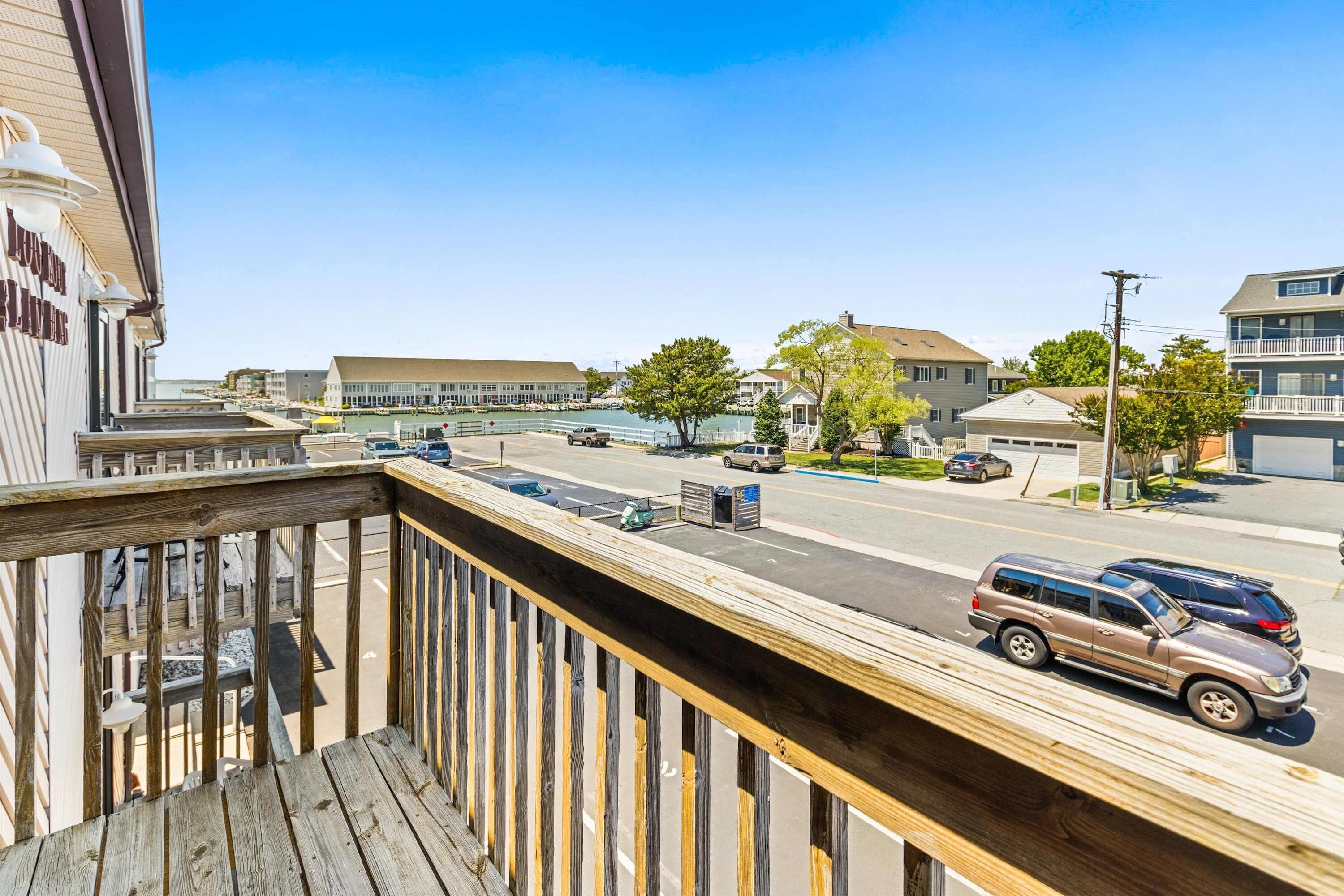A balcony overlooking a street with parked cars, buildings, and a clear sky.