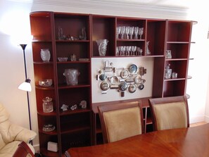 A dining area with a wooden table and chairs, surrounded by wooden shelves with glassware and decorative items.
