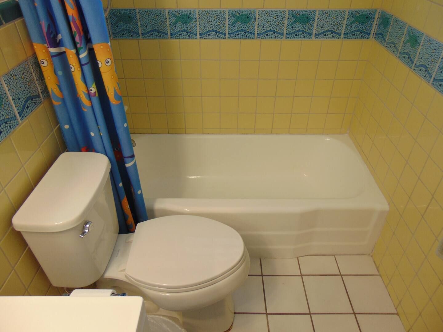 Un baño con inodoro, bañera y paredes cubiertas de azulejos amarillos.