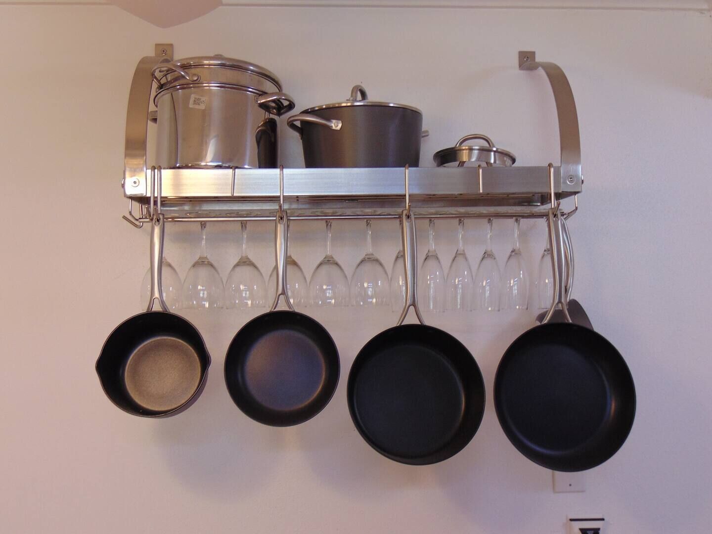 A kitchen with pots and pans hanging on a rack, and wine glasses below.