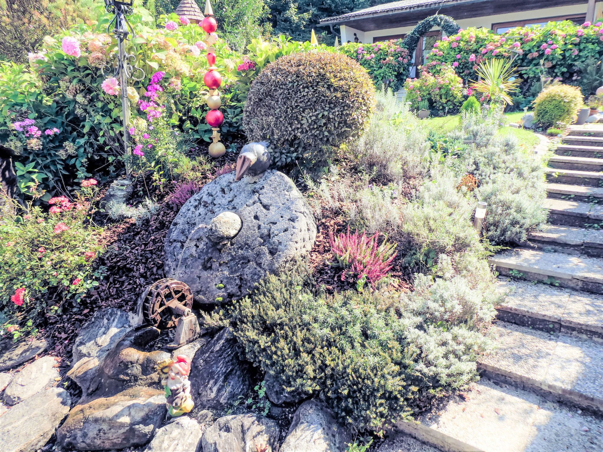 A garden with a water wheel, rocks, and various plants.