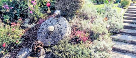 A garden with a water wheel, rocks, and various plants.