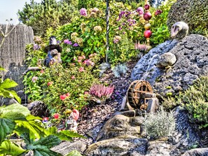 A garden with a water feature, a wooden wheel, and various plants. - Ferienwohnung Seeblick 2 by Interhome (Velden am Wörthersee)
