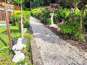 A garden pathway with decorative statues, a wooden fence, and flowering plants. - Ferienwohnung Seeblick 2 by Interhome (Velden am Wörthersee)