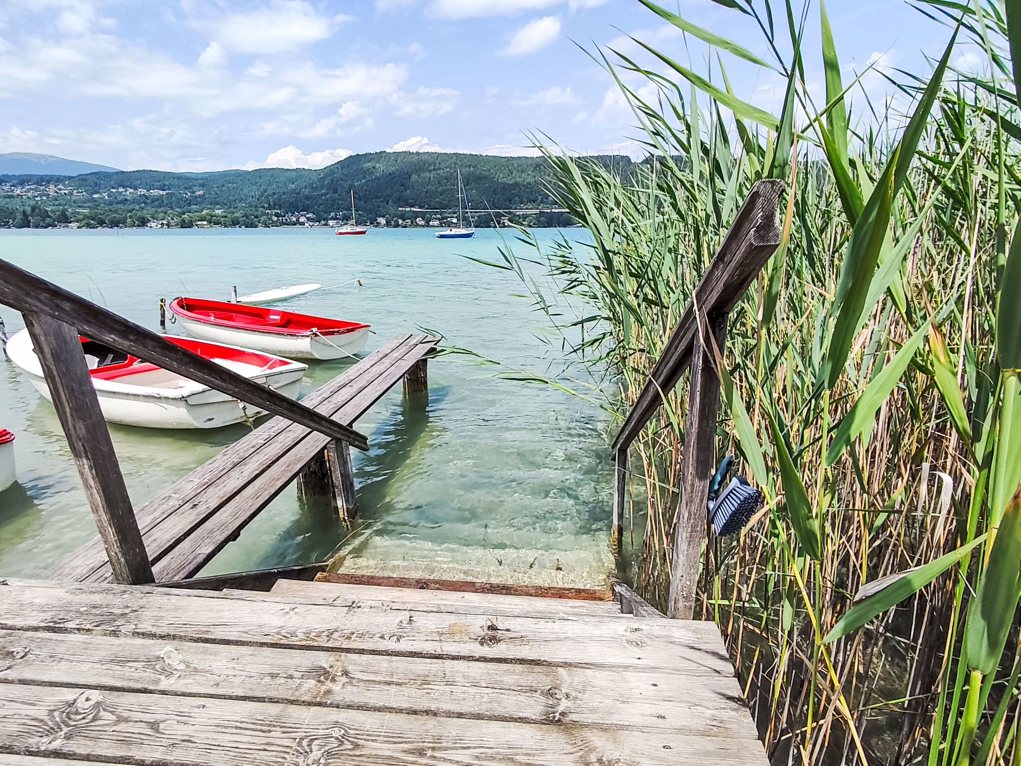 A wooden dock leading to a calm lake with boats and a distant mountain range.