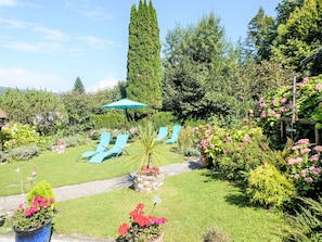 A garden with a pathway, a blue umbrella, and two lounge chairs. - Ferienwohnung Seeblick 1 by Interhome (Velden am Wörthersee)