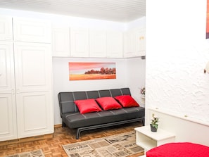 A room with a black sofa, red cushions, a painting, white cabinets, and a patterned rug. - Ferienwohnung Seeblick 1 by Interhome (Velden am Wörthersee)