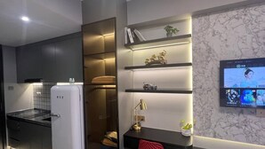 A modern kitchen with a white refrigerator, built-in shelves, and a TV mounted on the wall.