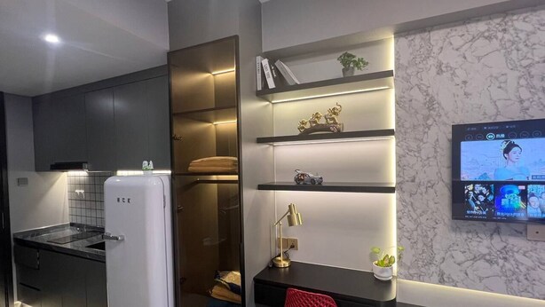 A modern kitchen with a white refrigerator, built-in shelves, and a TV mounted on the wall.