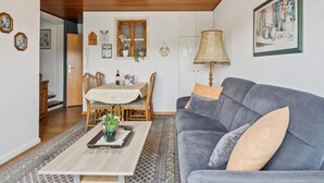 Ein Wohnzimmer mit Holzboden, einem Esstisch mit Stühlen, einer Couch und einer Lampe.
