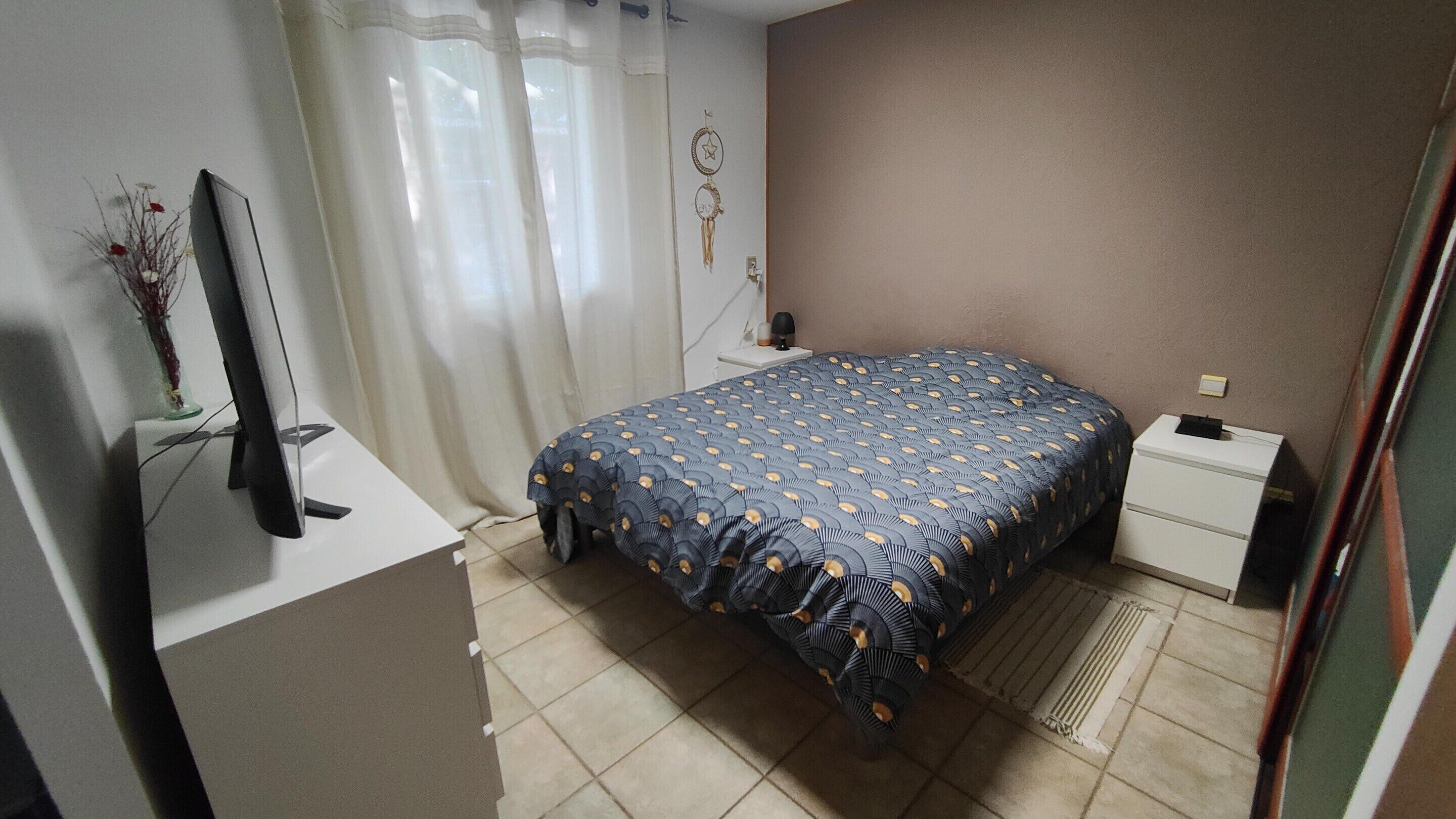 A bedroom with a bed, a desk, a chair, a TV, and a wall decoration.