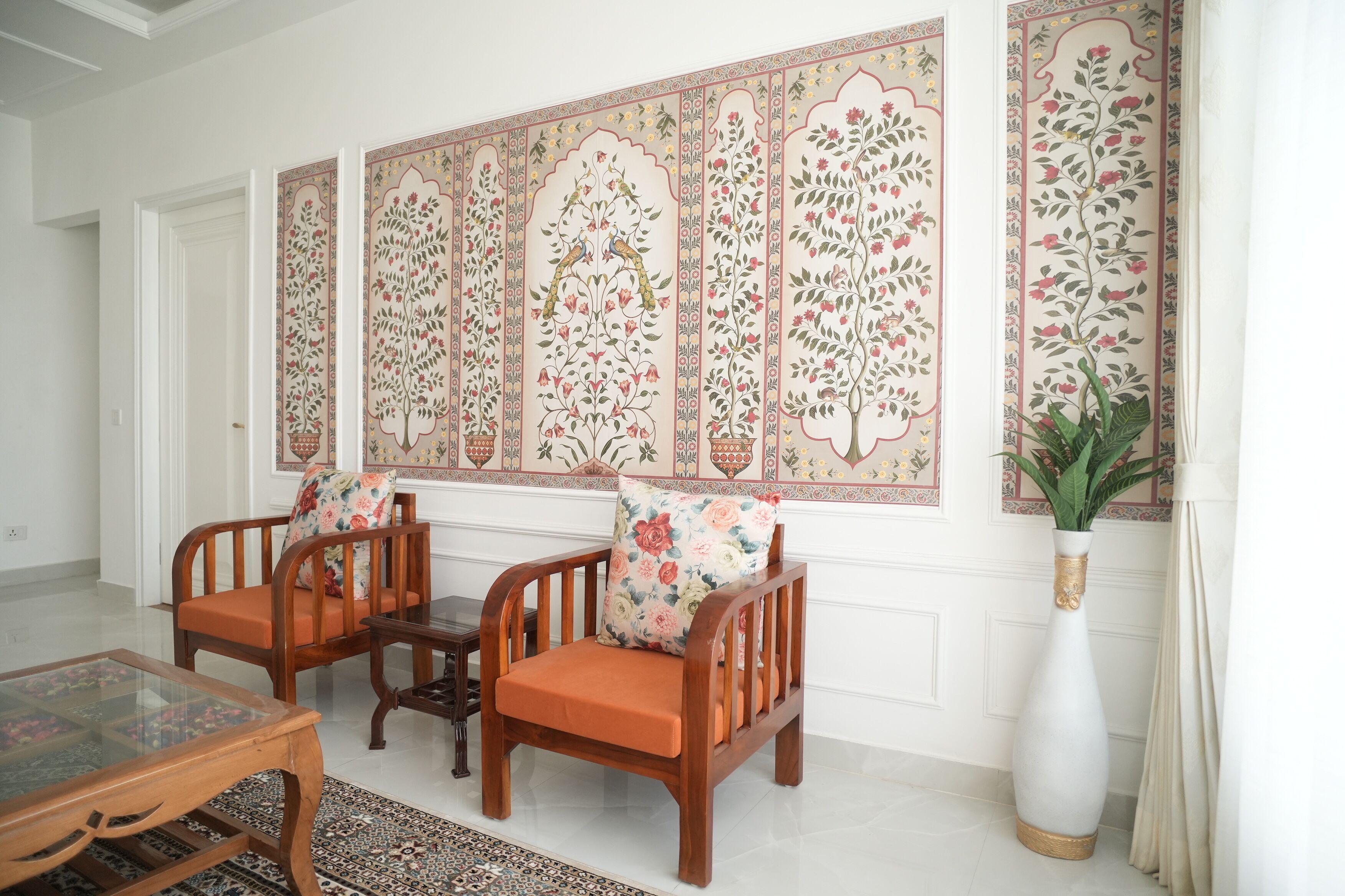 Una habitación con dos sillas de madera, una mesa de vidrio y un panel decorativo grande en la pared.