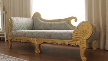 Un sofá antiguo con detalles dorados ornamentales y tapicería estampada en una habitación con suelo de madera y alfombra con diseño.