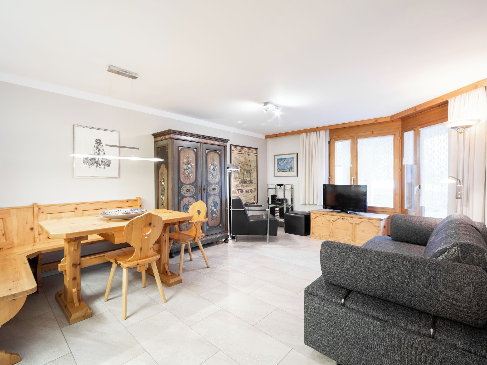 A living room with a wooden dining table, chairs, a grey sofa, and a TV.