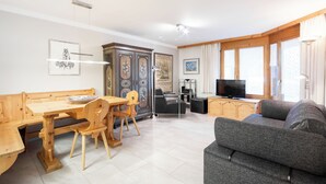 A living room with a wooden dining table, chairs, a grey sofa, and a TV. - Runca 752 by Interhome (Flims)