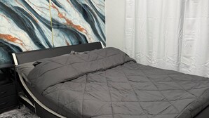 Une chambre à coucher moderne avec un lit, une table de chevet, un mur au motif évoquant le marbre et un rideau blanc.
