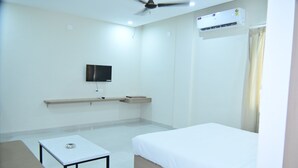 A hotel room with a bed, a desk, a television, and an air conditioning unit. - Hotel BR Residency (Bikaner)