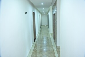 Um corredor comprido e estreito com piso de mármore e paredes brancas.