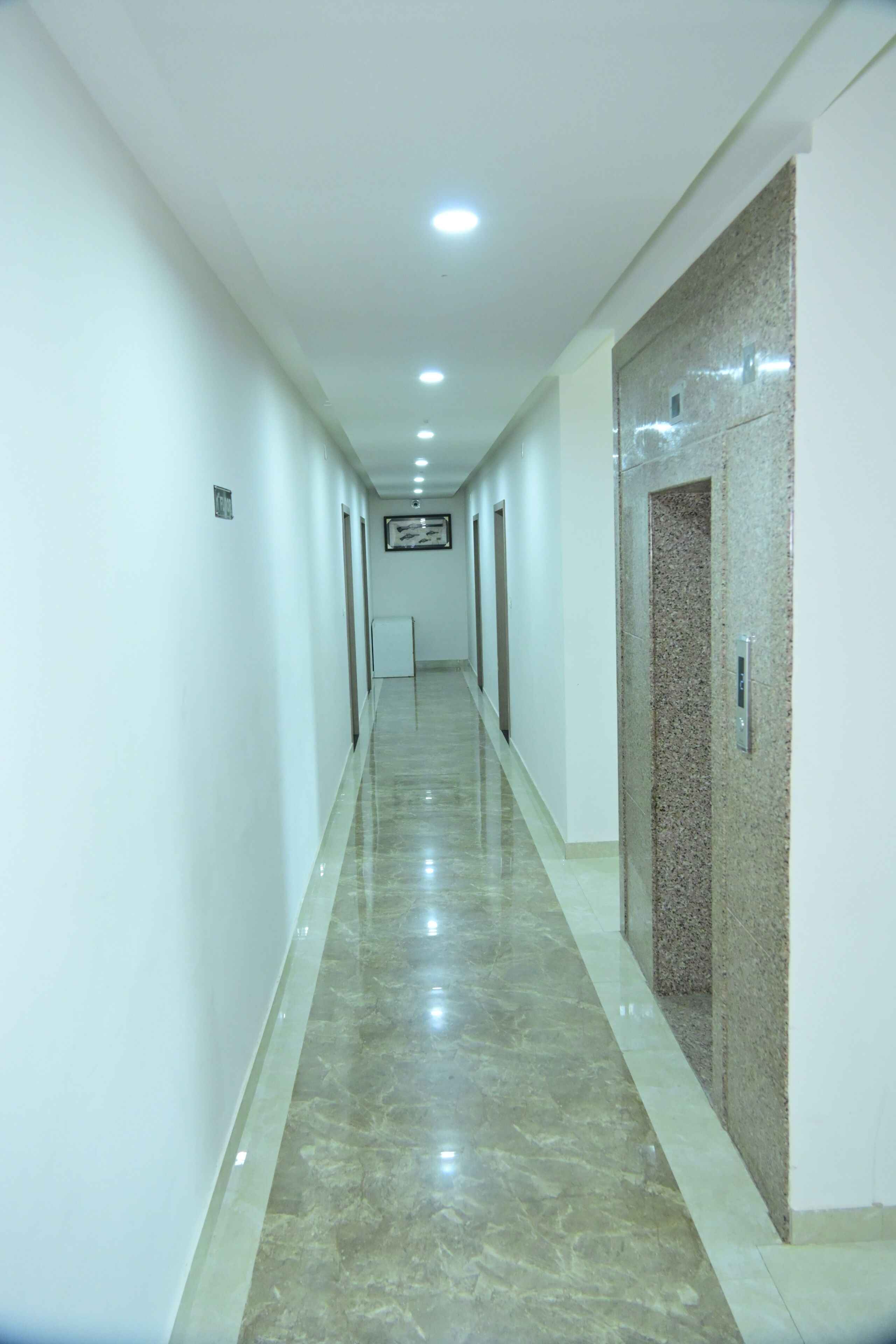 A long, narrow hallway with a polished floor, white walls, and a ceiling with recessed lighting.