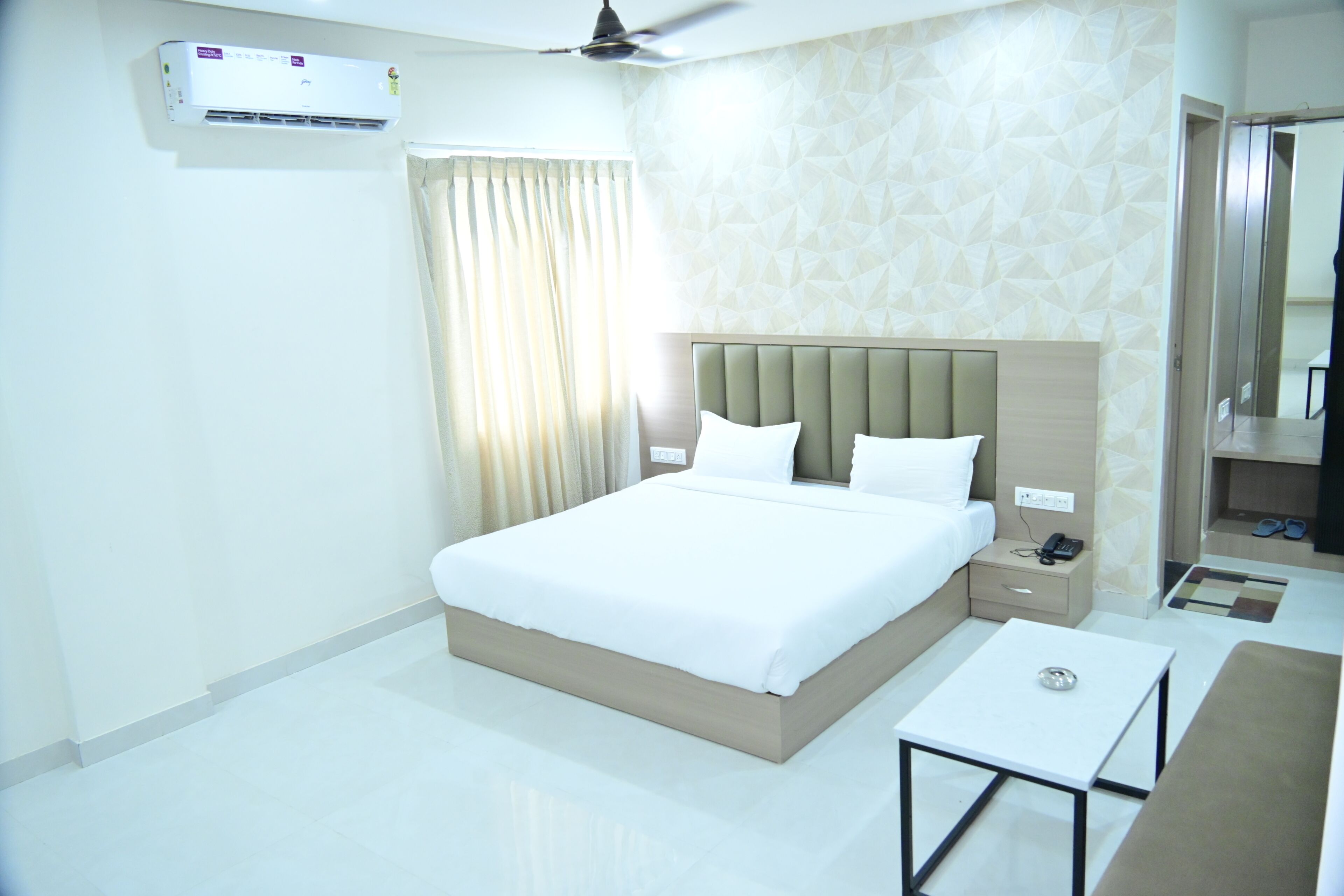 A hotel room with a bed, bedside table, and a small table with a lamp.