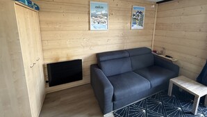 Huone, jonka seinät ovat puuta, siinä on harmaa sohva, pieni pöytä ja kaksi kehystettyä kuvaa.