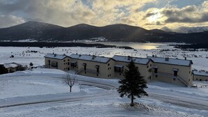 Lumipeitteinen maisema, jossa on rivi rakennuksia, kirkas taivas ja taustalla kohoavat vuoret.