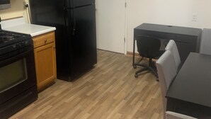 Une cuisine avec des meubles de rangement en bois, un réfrigérateur noir, une cuisinière et un coin repas comprenant une table et des chaises.