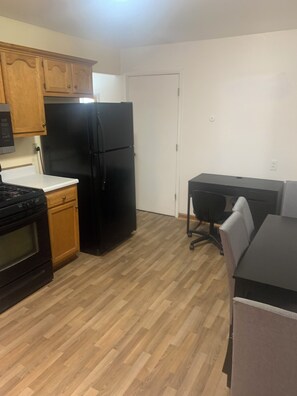 A kitchen with wooden cabinets, a black refrigerator, a stove, and a dining area with a table and chairs.