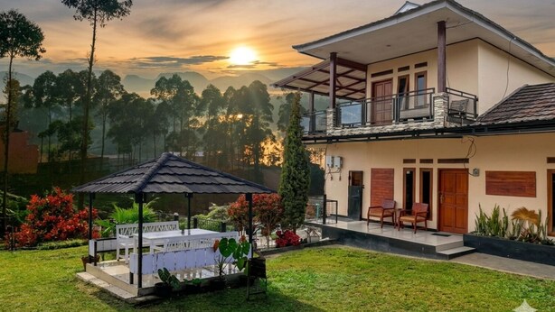 Ein zweistöckiges Haus mit Balkon, überdachter Terrasse und Blick auf den Sonnenuntergang über den Hügeln.