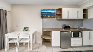 Eine kleine Küche mit Kühlschrank, Mikrowelle und Spüle. Ein Esstisch mit Stühlen und ein Gemälde an der Wand.