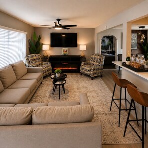 Ein Wohnzimmer mit Sofa, Sesseln, Couchtisch, Kamin, Fernseher und einer Bar.