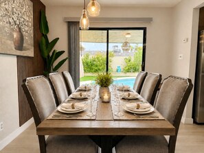 A dining area with a wooden table set for six, surrounded by upholstered chairs, with a view of a swimming pool outside. - Serene 4-bedroom house with AC in lovely Las Vegas with Private Pool and Sauna (Las Vegas)