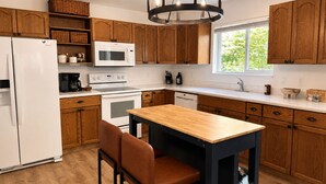 Une cuisine moderne avec des meubles en bois, un réfrigérateur blanc, un four à micro-ondes, une cuisinière et un coin repas comprenant une table et des chaises.