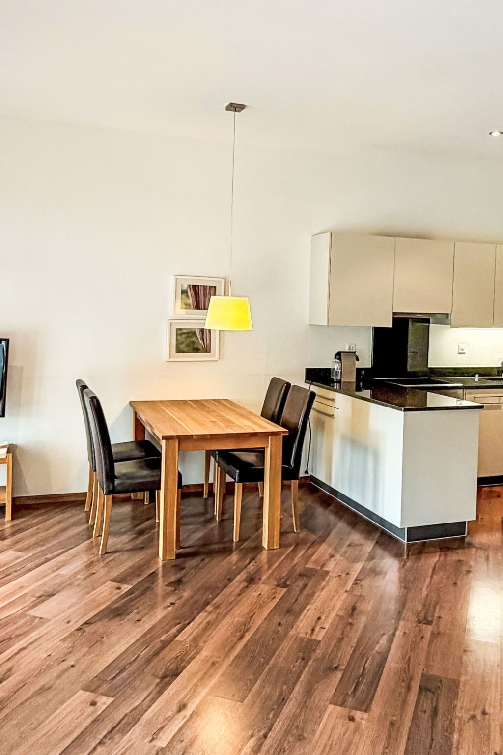 Una cocina moderna con una mesa y sillas de madera, una lámpara colgante amarilla y una pequeña isla con fregadero.