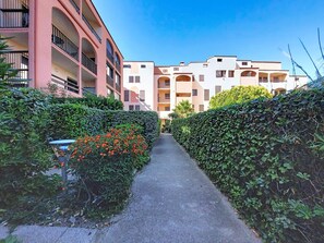 A narrow pathway flanked by neatly trimmed hedges and a row of multi-story buildings with balconies. - Le Tropique by Interhome (Saint Cyprien)